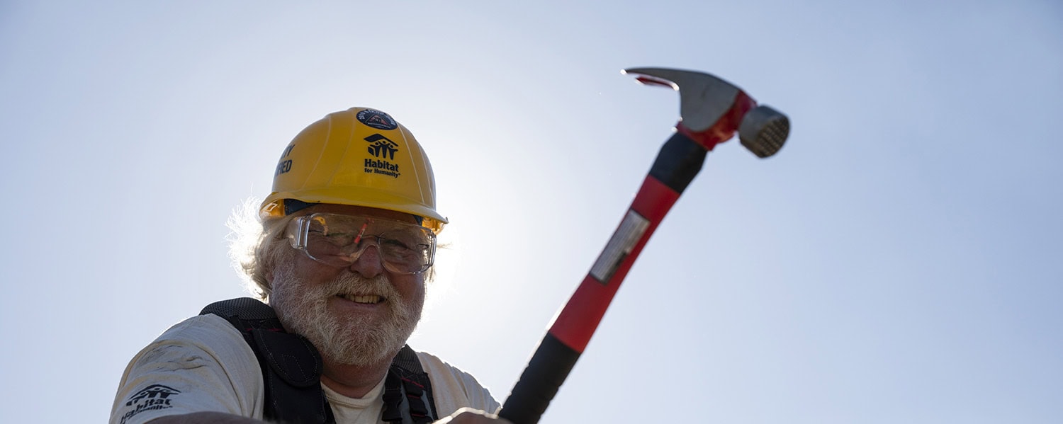 Man on roof with hammer in Habitat helmet